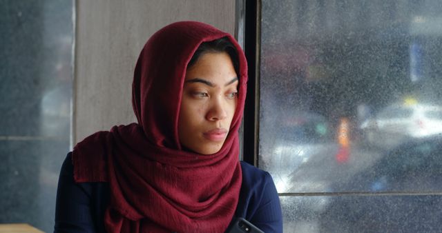 Contemplative Muslim Woman by Window with Smartphone - Download Free Stock Images Pikwizard.com