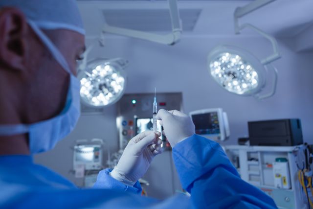 Rear view of male surgeon looking at needle in operation room at the hospital