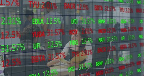 Business team discussing laptop with stock tickers reflected on glass wall, collaborating