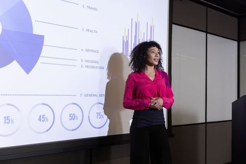 Professional Woman Presenting Data to Audience in Meeting Room