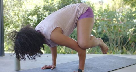 African american woman practicing arm-balance yoga on patio mat for outdoor wellness daily
