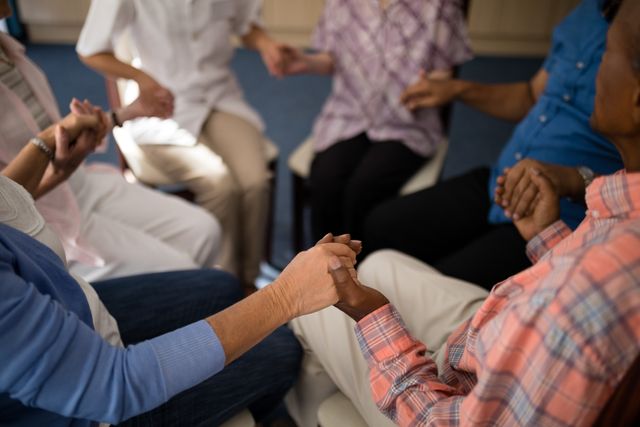 This image depicts seniors and a caregiver holding hands in a supportive circle at a retirement home. Ideal for use in healthcare, senior living, and community support contexts. It can be used to illustrate themes of unity, compassion, and elderly care in promotional materials, websites, and brochures.