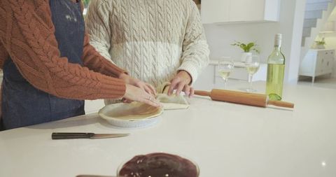 Couple attentively folding dough into pie pan at modern kitchen island