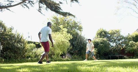 Diverse friends playing backyard soccer on sunny lawn with ball midair and vibrant greens
