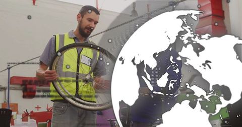Technician in Workshop Assessing Bicycle Wheel near Graphic Globe