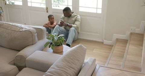 African american father and son sitting on floor sharing conversation by sunlit glass door