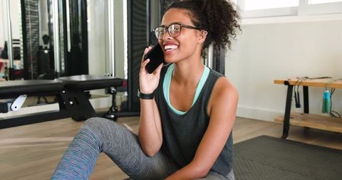 African American woman smiling and talking on smartphone while resting on gym mat