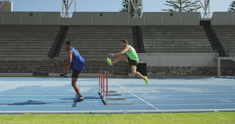 Two Athletes Hurdle Jumping on Blue Running Track