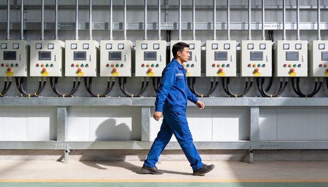 Industrial technician walking along electrical control panels in modern plant corridor