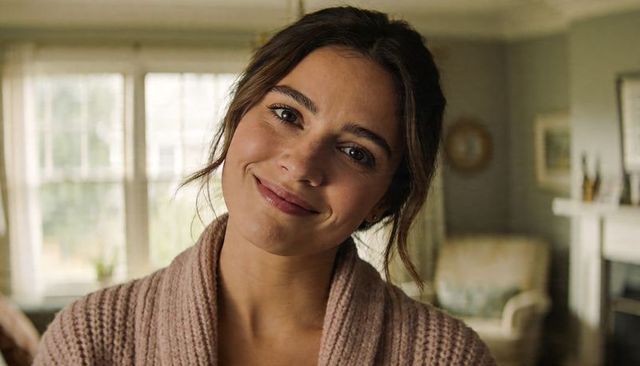 Smiling woman wearing chunky knit cardigan in cozy sunlit living room, warm lifestyle portrait