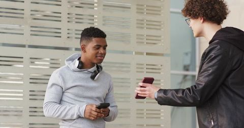Young diverse friends sharing smartphones near modern slatted wall, urban social connection