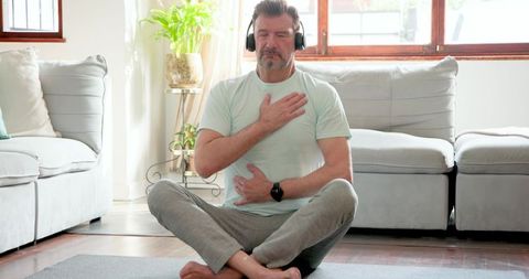 Senior man meditating with headphones in cozy living room