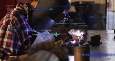 Female welder using tig torch at workshop bench wearing helmet and plaid shirt