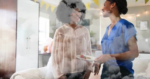 Smiling women exchanging dessert plate at home party with bunting, balloons and pastries