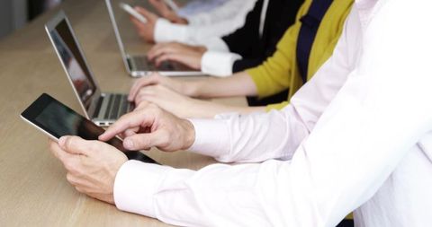 Business team tapping tablet and typing on laptops during collaborative meeting at office table