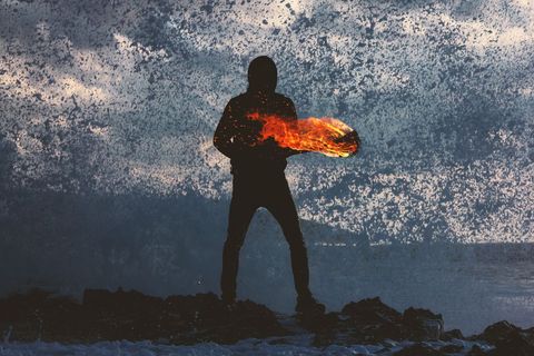 Silhouette with Fiery Element Against Powerful Ocean Waves