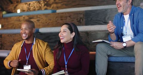 Diverse coworkers smiling, taking notes during collaborative workshop on wooden benches
