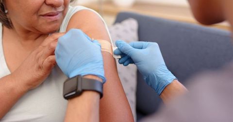 Caregiver applying bandage after vaccination for senior woman at home