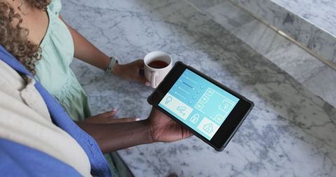 Multiracial Couple Using Smart Home Tablet While Holding Coffee on Marble Counter
