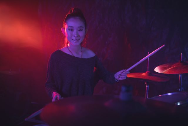Portrait of smiling female drummer playing drum kit in illuminated nightclub