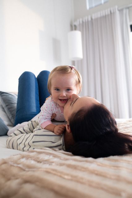 Happy caucasian mother lying on her back on bed kissing smiling baby daughter - Download Free Stock Photos Pikwizard.com
