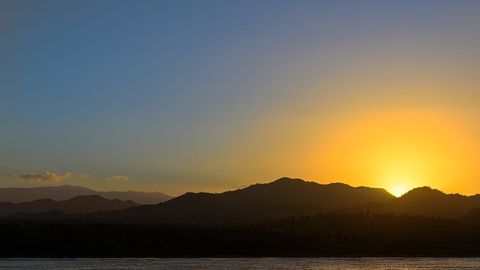 Golden Sunset Behind Mountain Silhouettes Over Calm Ocean Horizon