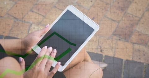 Woman holding tablet on outdoor steps showing financial graph overlay for mobile trading