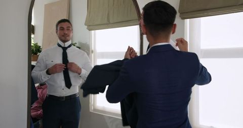 Groom adjusting tie in mirror before wedding