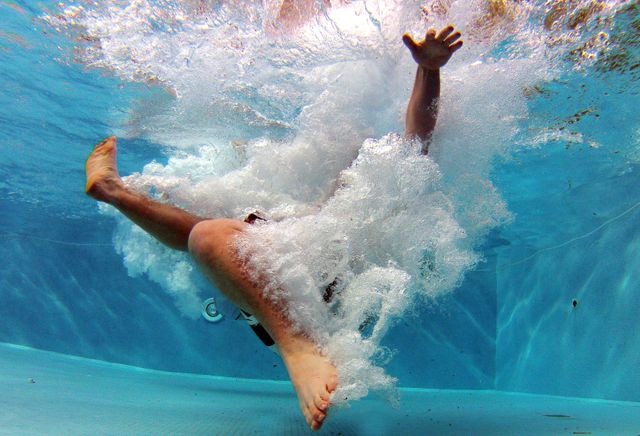 Person diving into swimming pool, creating big splash underwater. Perfect for summer activities, travel brochures, vacation highlights, and sports-related content. Ideal for use in promotional material for swimming pools or leisure centers.