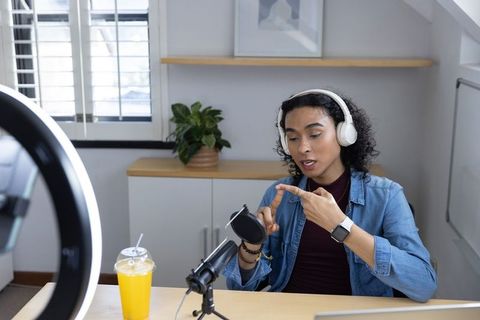 Non-binary creator recording podcast in bright home studio with headphones and microphone