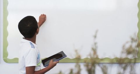 Boy in Classroom Engaging with Tablet at Whiteboard Indoor
