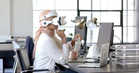 Woman wearing vr headset at office desk with laptop