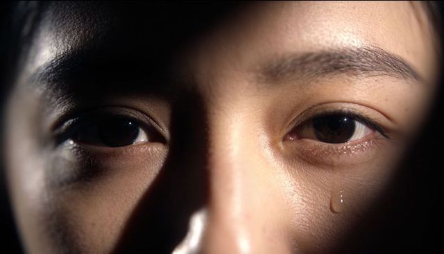 Close-up female face single tear dramatic chiaroscuro lighting emotional portrait