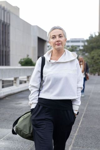 Mature professional woman walking urban plaza carrying duffel bag and wearing athleisure