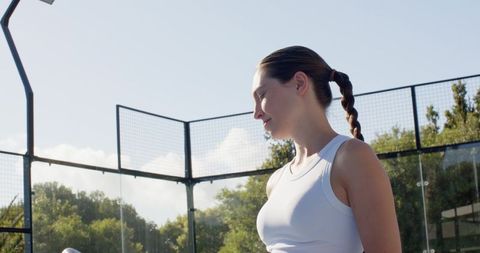 Young woman athlete standing on outdoor racket court holding racket handle and concentrating