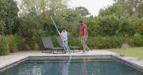 Father and son cleaning pool together on sunny day