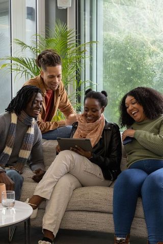 Friends gathering on sofa, sharing tablet and laughing in cozy living room