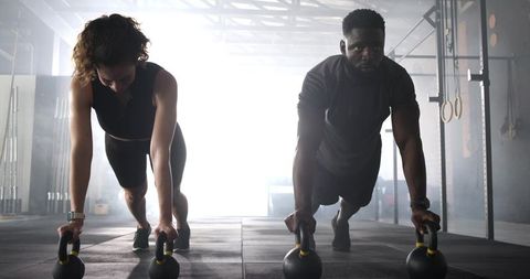 Diverse workout partners powering through kettlebell push-ups in modern gym