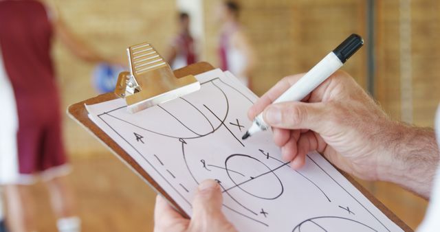 Hands of basketball coach drawing diagram on clipboard in the basketball court