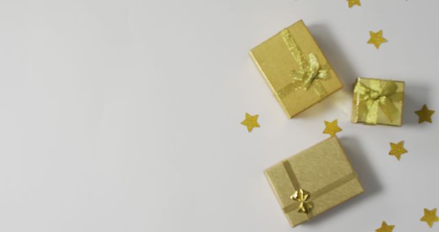 Three golden gift boxes decorated with bows are placed on a white background, surrounded by gold star confetti. Perfect for holiday greeting cards, festive decorations, birthday party invitations, or celebratory events.