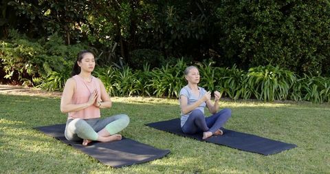 Senior and middle-aged asian women practicing seated yoga in sunlit garden for relaxation
