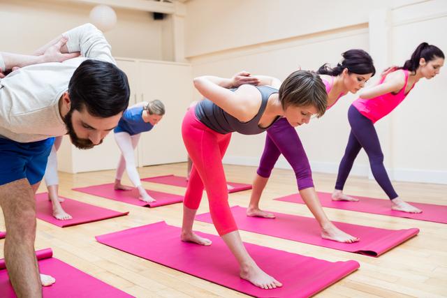 Group of people performing pyramid pose yoga exercise in the fitness studio