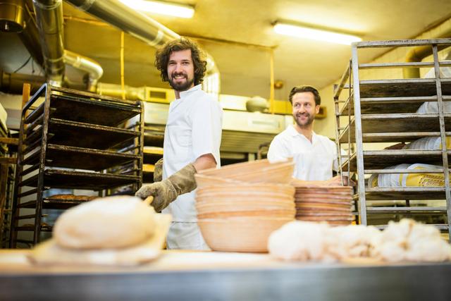 Portrait of two smiling bakers preparing bread in bakery kitchen