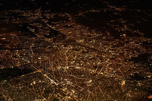 Aerial view of a city's illuminated landscape at night, showcasing a vibrant and bustling urban area. Ideal for use in articles, presentations, or advertisements related to urban planning, night city life, infrastructure, and electricity consumption. The glowing patterns of roads and buildings highlight the complexity and connectivity of modern cities.