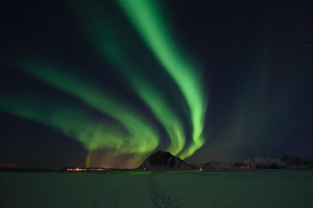 This stock photo beautifully captures the Northern Lights over a snowy landscape and mountains at night. It shows the stunning Aurora Borealis with vivid green lights dominating the sky, providing a sense of serenity and awe. Perfect for travel blogs, science articles, nature magazines, or wallpapers.