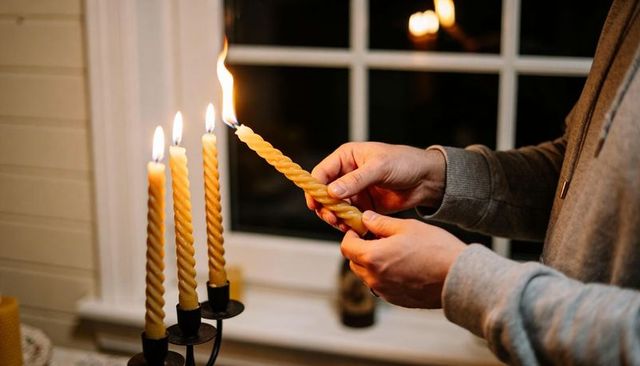 Lighting twisted beeswax candles at window hands creating warm cozy nighttime glow