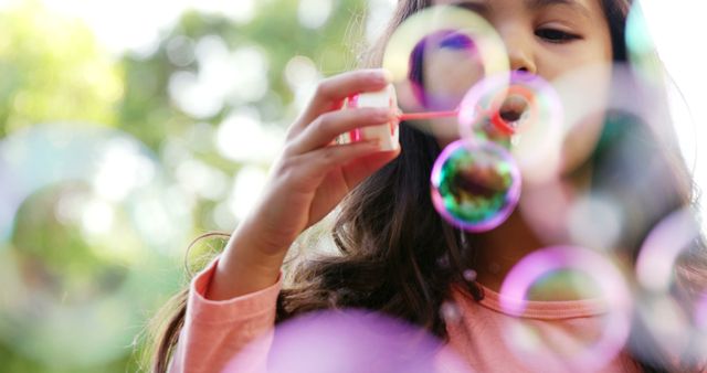 Young girl blowing colorful soap bubbles outdoors. Perfect for depicting playful childhood moments, advertisements for children’s toys, summer activities, or educational materials about outdoor play.