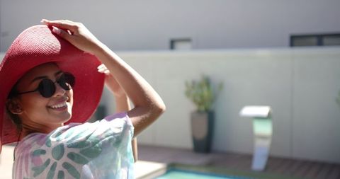 Smiling Woman in Red Hat Relaxing by Poolside on Sunny Day
