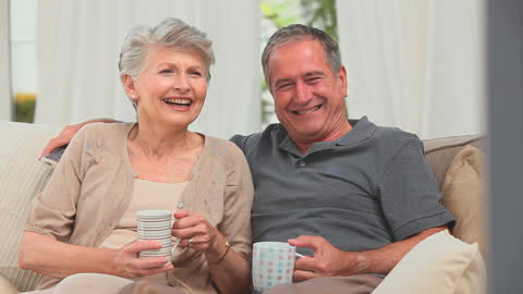 Mature Couple Relaxing on Sofa Watching Television Together