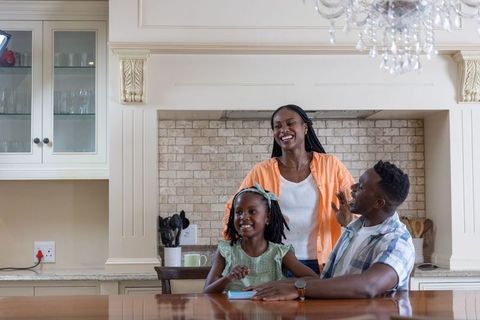 African american family enjoying morning at kitchen table, mother smiling, daughter writing